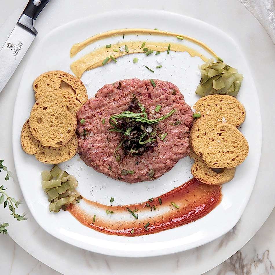 Özenle doğranmış taze dana eti, kapari, acı sos ve çıtır patateslerle sunulan Steak Tartar.