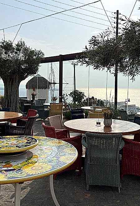 Nusret Mykonos'ta Ege Denizi'ne bakan, Akdeniz esintili renkli masa ve sandalyelerle döşenmiş açık hava yemek alanı.
