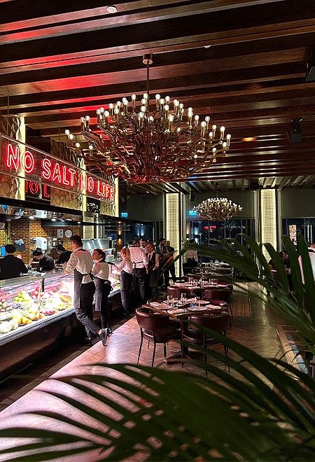 Nusr-Et Doha’da lüks yemek deneyimi, avizeler ve 'No Salt No Life' neon yazısıyla canlı bir iç mekan, üst düzey bir steakhouse atmosferi sunuyor.